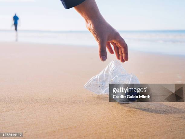 hand picking up plastic bottle at beach. - plastic pollution beach stock pictures, royalty-free photos & images