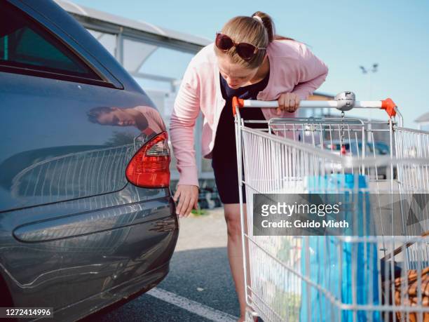 woman with face mask checking car after car accident at supermarket. - scratched car stock pictures, royalty-free photos & images