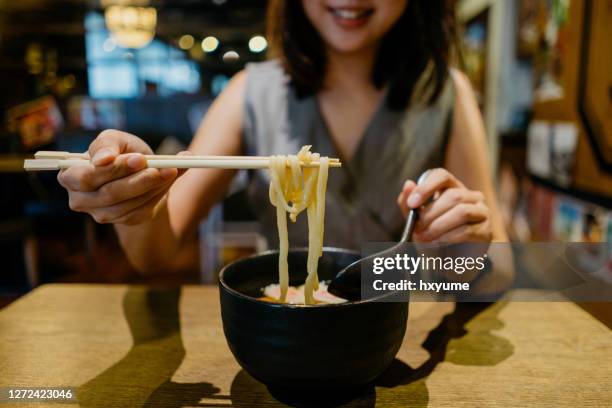 junge asiatische frau genießen eine schüssel von japanischen kitsune udon im restaurant - udon noodles stock-fotos und bilder