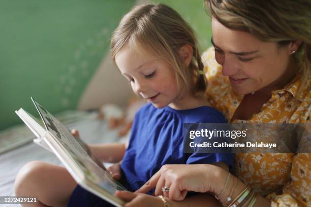 a mother reading a book to her daughter in the bedroom - bedtime story book stock pictures, royalty-free photos & images