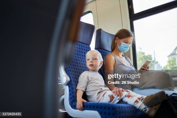 um menino loiro senta-se ao lado de sua mãe, que está usando uma máscara protetora ou máscara cirúrgica, no trem e olha para a esquerda - driving mask - fotografias e filmes do acervo