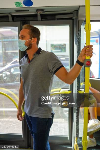 young man catching bus safety bar with surgical mask - midsagittale vlak stockfoto's en -beelden