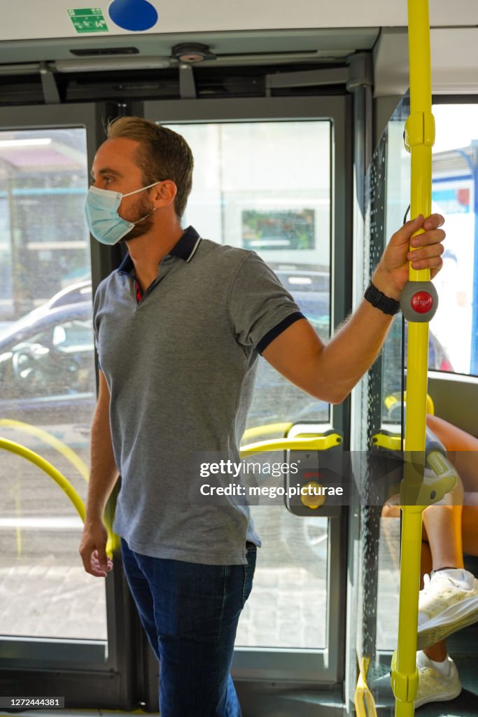 Young man catching bus safety bar with surgical mask
