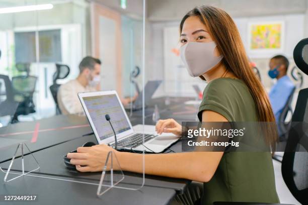 imprenditrice che usa le cuffie e lavora su laptop in ufficio indossando una maschera protettiva per il viso - cloth face mask foto e immagini stock