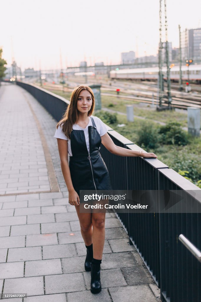 Full length portrait of young hispanic woman aged 20-24 years in a mini dress leaning onto a railing looking at camera
