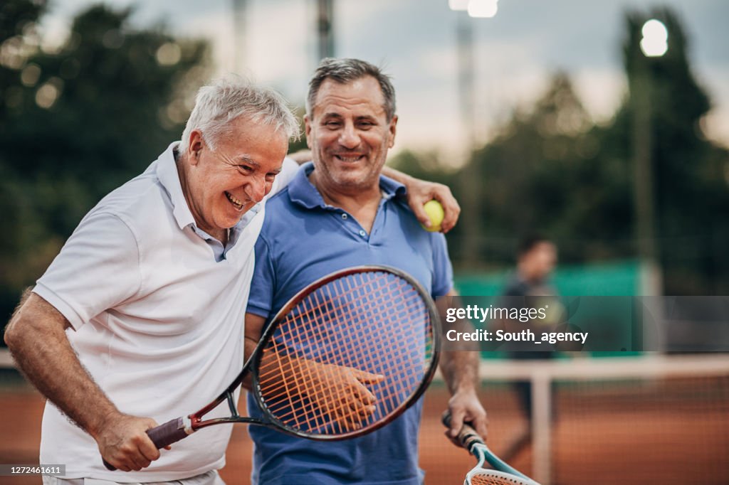 Zwei fröhliche Senioren sprechen beim Gehen auf dem Tennisplatz im Freien