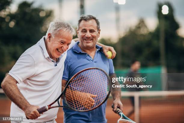 twee vrolijke hogere mensen die terwijl het lopen op de openluchttennisbaan spreken - retirement enjoy active stockfoto's en -beelden