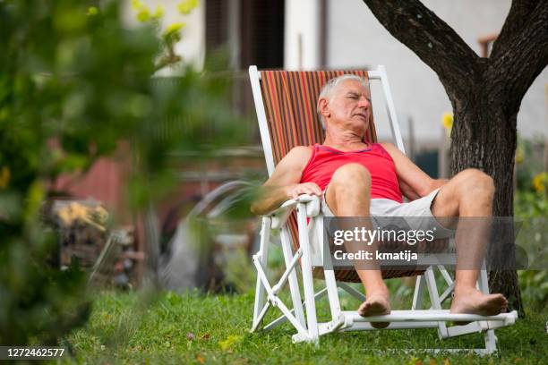 hombre adulto mayor cansado siesta en la silla del salón en el patio trasero - silla de playa fotografías e imágenes de stock