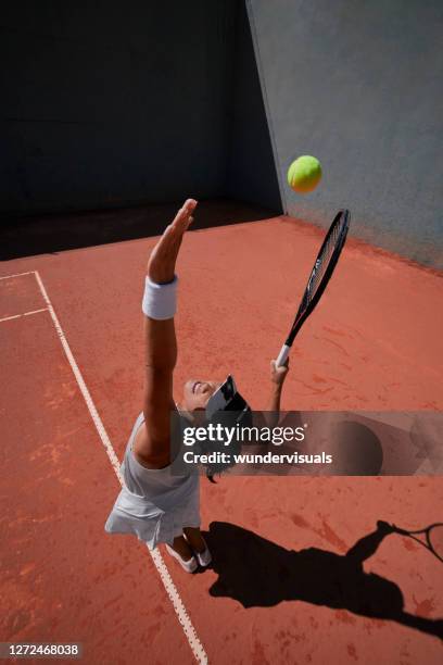 frau serviert ball während tennis-match auf sandplatz - tennisturnier stock-fotos und bilder