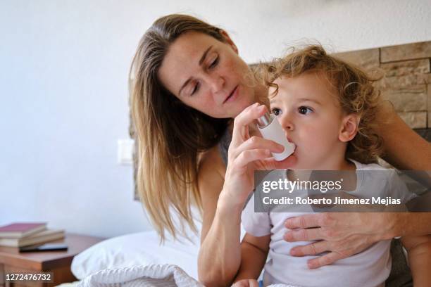 woman with son using an inhaler in bedroom - inhalador-preventivo-del-asma fotografías e imágenes de stock