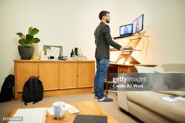 young man working remotely at a standing desk in his living room - home office ergonomics stock pictures, royalty-free photos & images