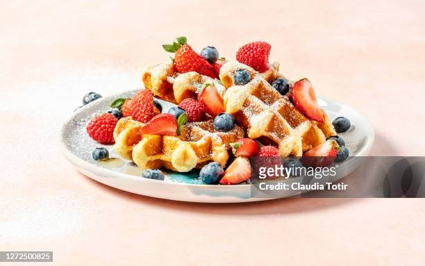 a plate of waffles with berries on peach background - belgium waffles stock pictures, royalty-free photos & images