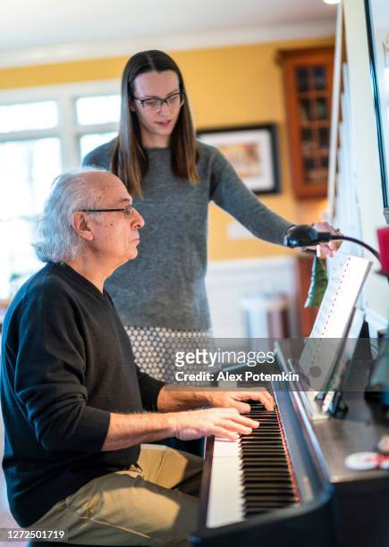 l'anziano uomo di 72 anni dai capelli bianchi, un padre, che suona il pianoforte, e sua figlia adulta lo aiutano girando le pagine della partitura. - 25 29 years foto e immagini stock