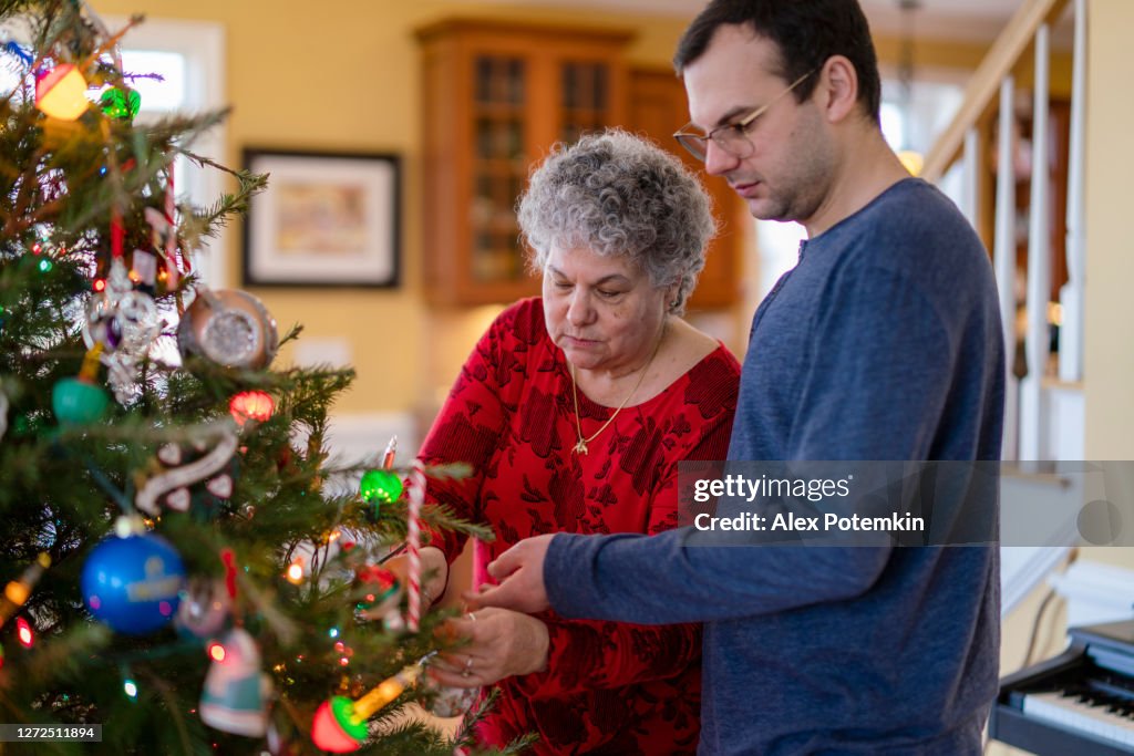 Senior 65-years-old woman decorating Christmas Tree together with her adult son