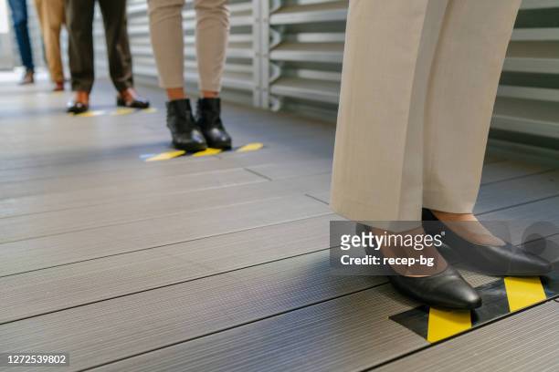 business people waiting in line behind social distancing sign on floor - social distancing stock pictures, royalty-free photos & images