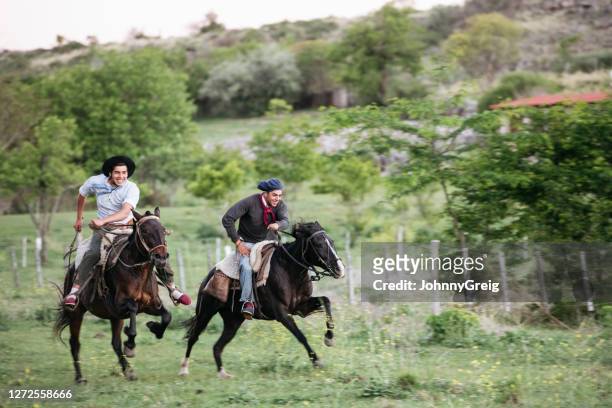 young gauchos grinning while racing on horseback - gaucho argentina stock pictures, royalty-free photos & images