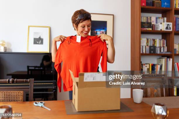 woman looking at online purchased clothing at home - shopping online stockfoto's en -beelden