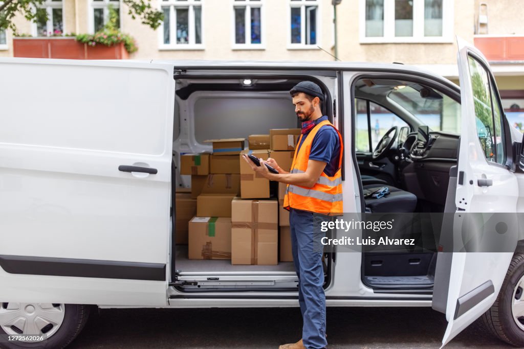 Delivery man using digital tablet by van