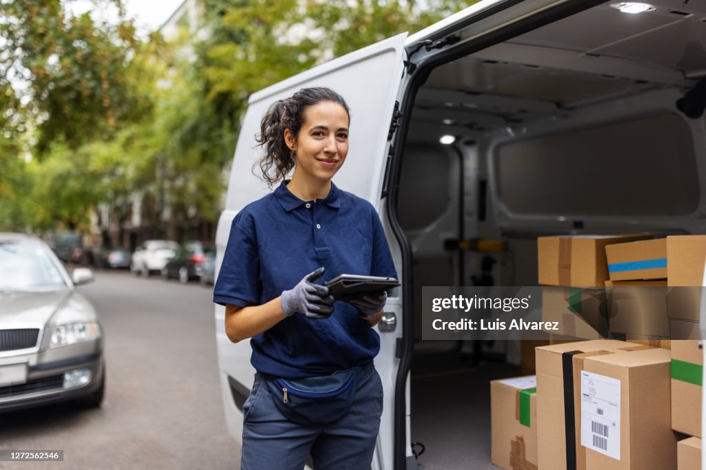 Female courier worker standing by delivery van