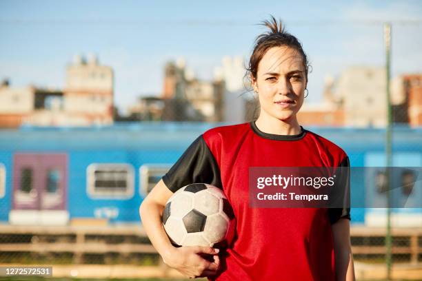 een vrouwelijk voetbalvoetballerportret dat een bal onder haar wapen houdt. - womens soccer stockfoto's en -beelden