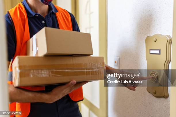 postal worker doing a home delivery of parcel - ringing doorbell - fotografias e filmes do acervo