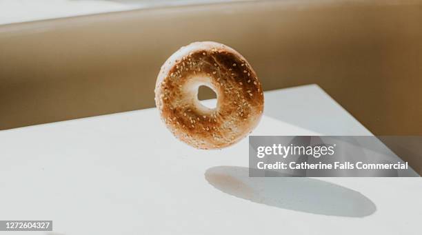 sesame seed bagel in mid-air above a white table - bagel stock-fotos und bilder