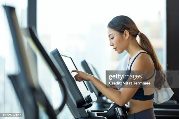 side view of an attractive young woman selecting workout program on a treadmill in a gym. - center athlete stock pictures, royalty-free photos & images