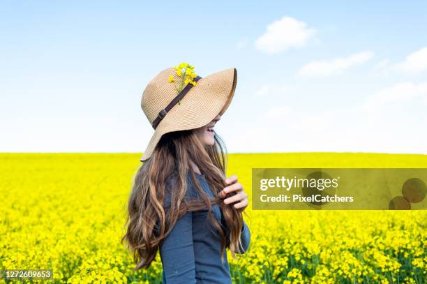 zijaanzicht jonge vrouw die zonnehoed op gebied van gele bloemen draagt - canola stockfoto's en -beelden