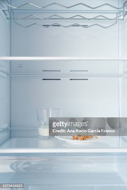a glass of milk half empty and a plate with crumbs inside a cold and empty fridge - inside fridge stockfoto's en -beelden