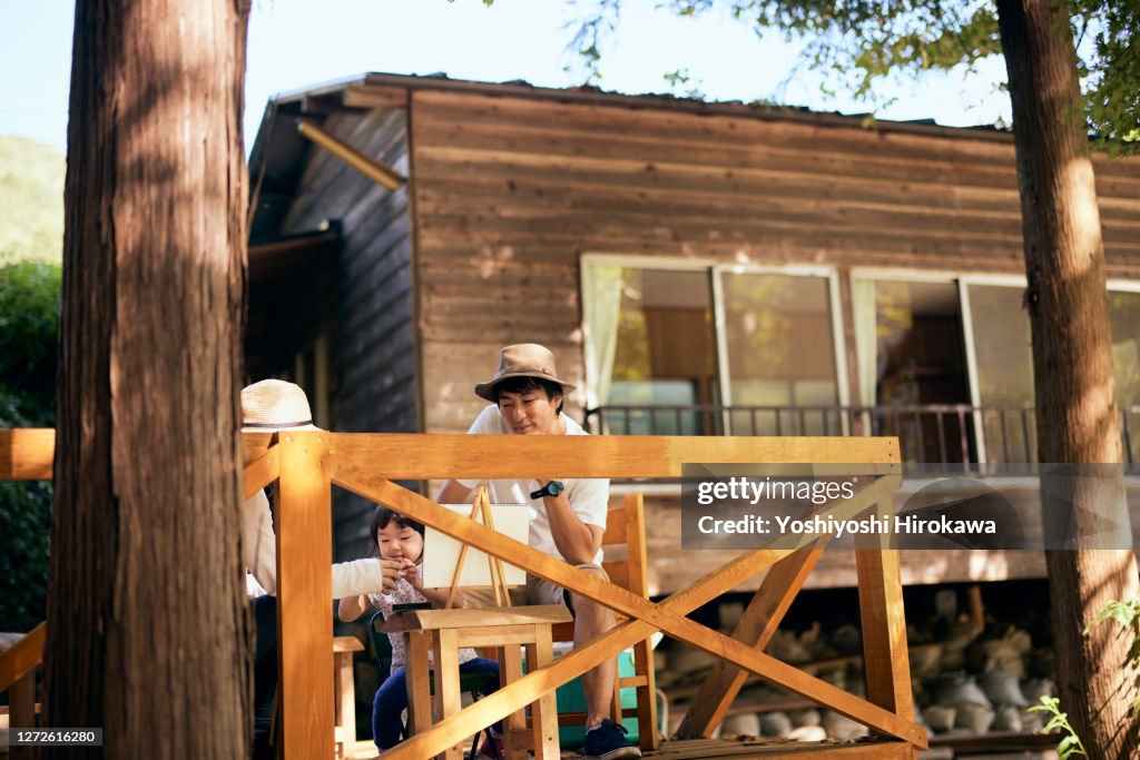 Real daughter and parents painting on a wooden deck at a campsite