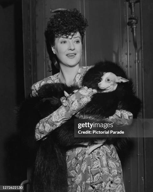 American burlesque entertainer and actress Gypsy Rose Lee with her pooch Topsy wrapped in a black fur shawl arrive in New York City, US, 1944.