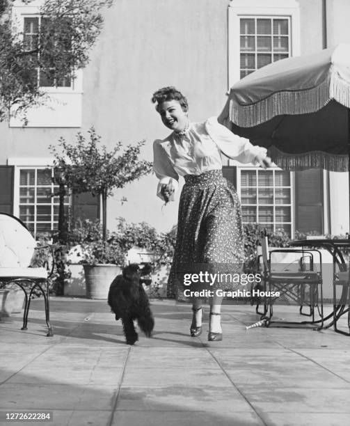 American actress Anne Baxter running with her Poodle dog Shoo Fly, US, circa 1950.