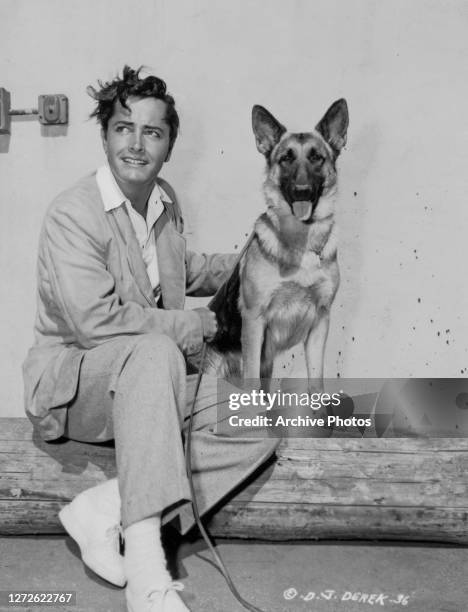 American actor, director, screenwriter, producer and photographer John Derek with a German Shepherd dog, US, circa 1949.