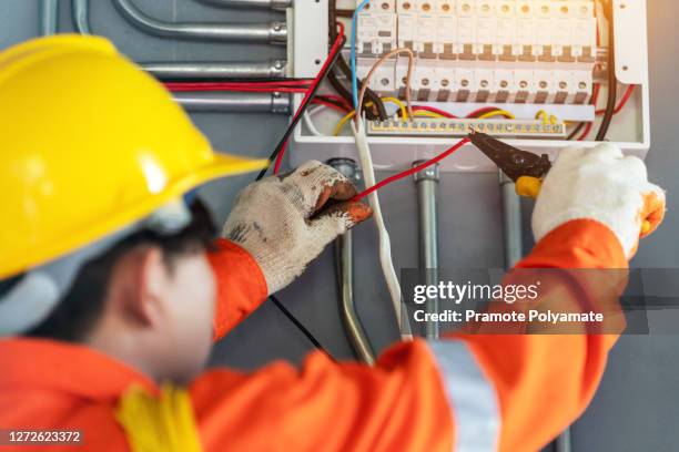 asian electrician in safety wear a uniform and helmet at work. reinstallation of residential electrical system. - schaltschrank stock-fotos und bilder