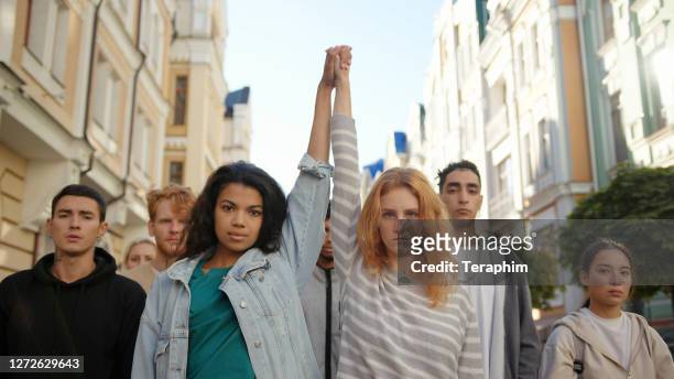 due donne multirazziali che si tengono per mano e le sollevano nella protesta di massa contro il razzismo - dimostrazione di protesta foto e immagini stock