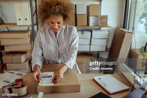 onderneemster die streepjescodeetiket op leveringspakket plakt - packing boxes stockfoto's en -beelden