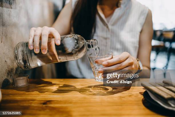 midsection of young asian woman pouring water from bottle into the glass in a restaurant - chorro agua fotografías e imágenes de stock