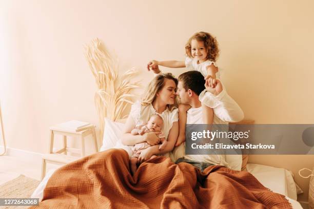 happy young family with two children resting in bed in a cozy home, mom dad child and baby - good night kiss stock-fotos und bilder