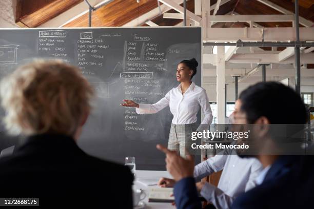 young african businesswoman giving a chalkboard presentation to colleagues - executive board meeting photos et images de collection