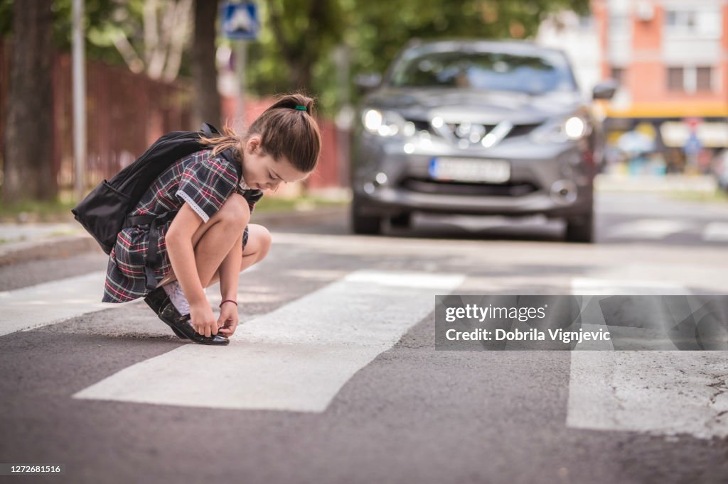 Girl fixing her shoeson at the crosswalk