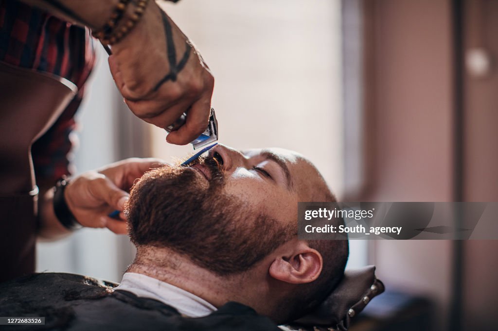 Jeune barbier mâle travaillant sur la barbe d’un client