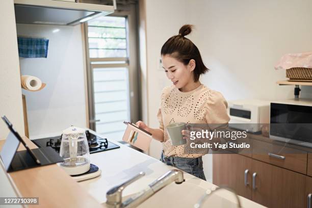 woman using a using smart phone in the kitchen - the japanese wife stock pictures, royalty-free photos & images