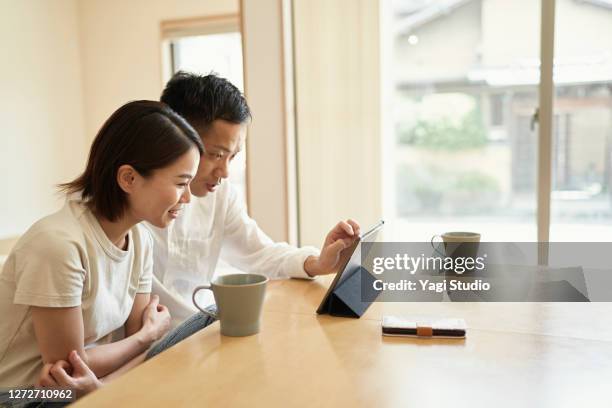 asian couple using a digital tablet in living room. - pareja de mediana edad fotografías e imágenes de stock