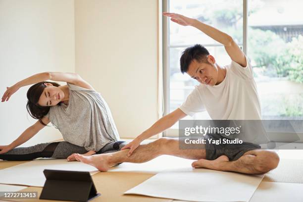 asian couple stretching exercises with digital tablet in the japanese-style room at home. - couple doing yoga stock pictures, royalty-free photos & images