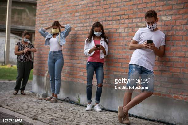 group of people standing socially distant and waiting for the bus on the street - social distancing line stock pictures, royalty-free photos & images