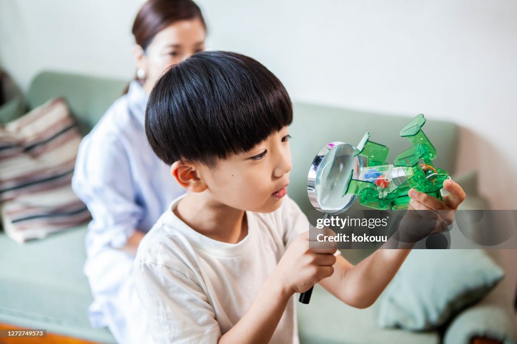 A boy watching a robot toy with a magnifying glass and a mother watching over it