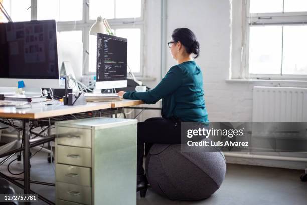 businesswoman sitting on a ball chair and coding - ergonomie stockfoto's en -beelden