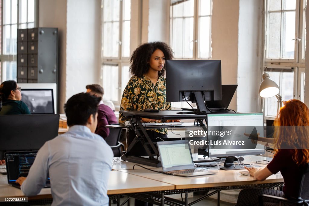 Woman working on computer at ergonomic standing desk in office