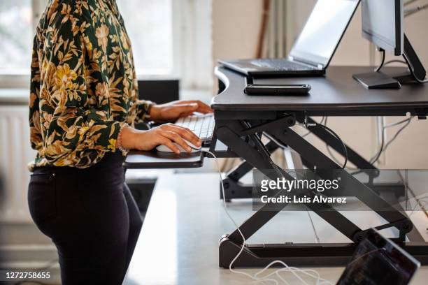 woman working at a standing desk in office - ergonomie stock-fotos und bilder