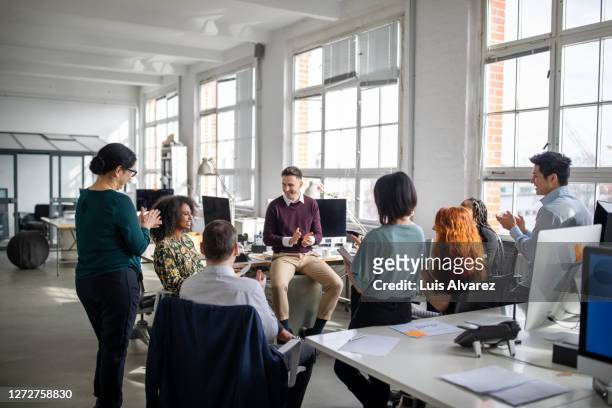 business team clapping for a female colleague in meeting - nuova impresa foto e immagini stock